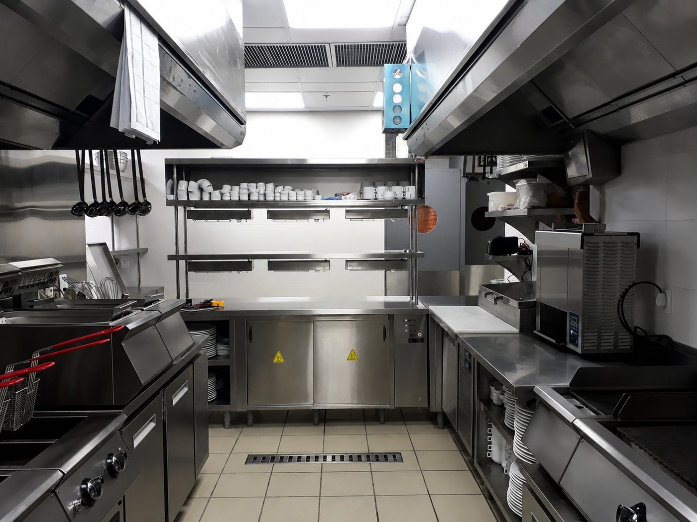 Cozinha profissional completa em operação, com linha de cocção, coifa e bancadas em aço inox
